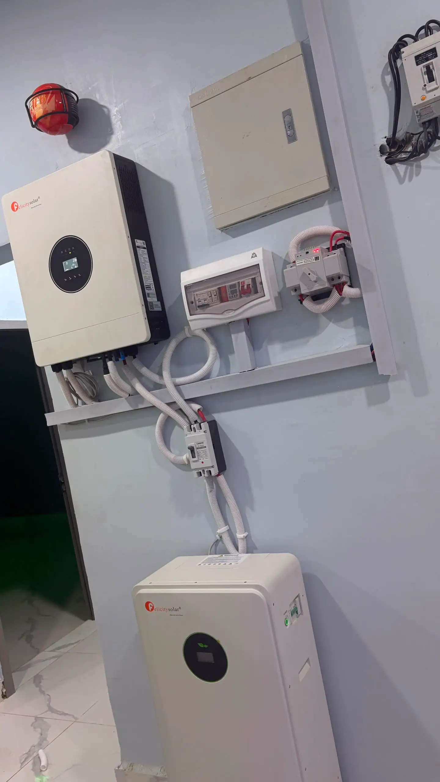 A wall-mounted hybrid inverter and distribution box above a floor-standing lithium battery.