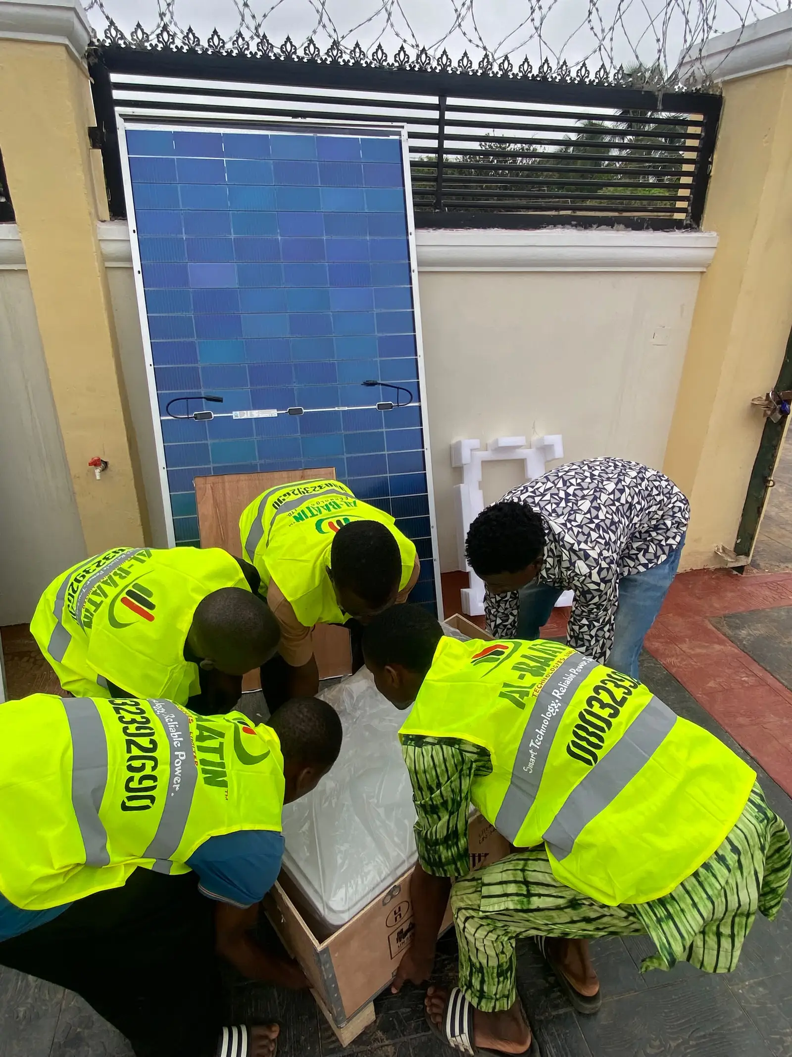 The crew unpacking solar panels against a compound wall before installation.