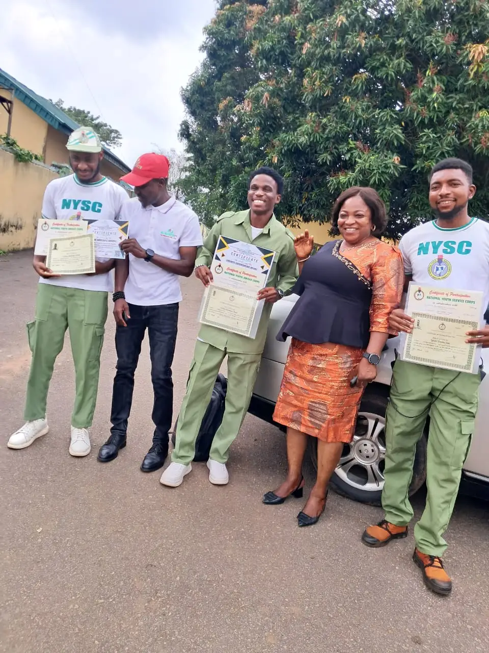 Three corps members holding their NYSC certificates of participation alongside Al-Baatin and Mrs Magaret Omaji, NYSC camp official.
